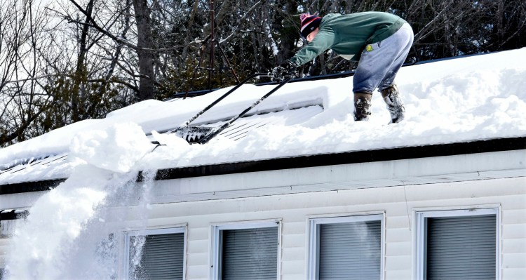 Trafton Gilbert stretches to dump snow over the slippery edge of a home in Sidney on Sunday. Gilbert was clearing the foot of snow to make room for the several inches of snow forecast to fall Monday. 
