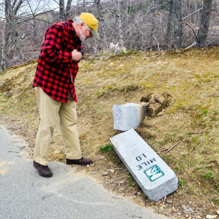 Paul Daiute looks at the tipped over one mile marker of the Kennebec River Rail Trail on Tuesday in Augusta.
