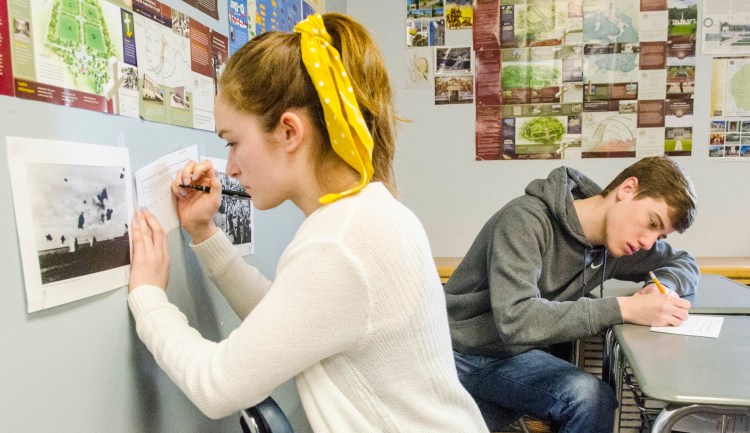 Students Laura Ireland, left, and Aric Belanger make notes on what they think is happening in World War II photos posted around Shane Gower's classroom on Wednesday at Maranacook Community High School in Readfield.