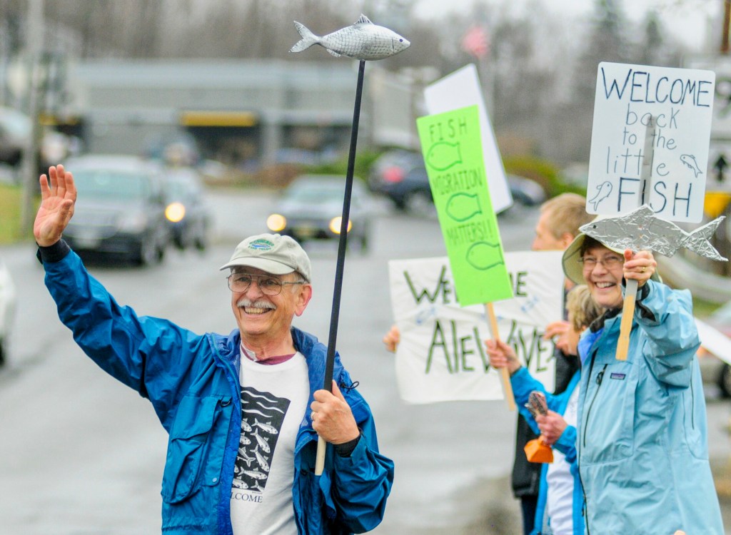 People wave signs and wooden fish and ring bells Saturday on Bridge Street on Saturday in Gardiner in observance of Earth Day. They also cleaned up the banks of Cobbosseecontee Stream. 