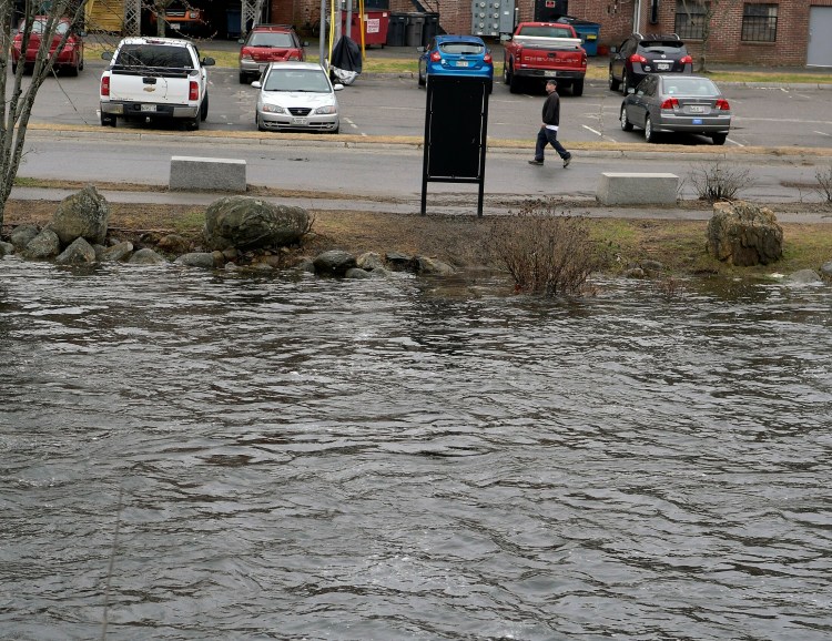 The swollen Cobbosseecontee Stream rises up the banks Sunday to the edge of a parking lot in downtown Gardiner.