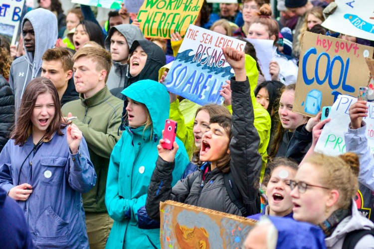 People yell and hold signs during a climate change rally Tuesday on the plaza between the Burton M. Cross State Office Building and the Maine State House in Augusta.