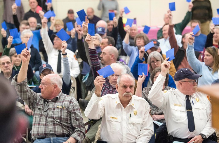 Tim Theriault, China's fire chief, front row center, and Richard Morse, right, cast their votes during the annual town meeting at the China Middle School in April 2019.