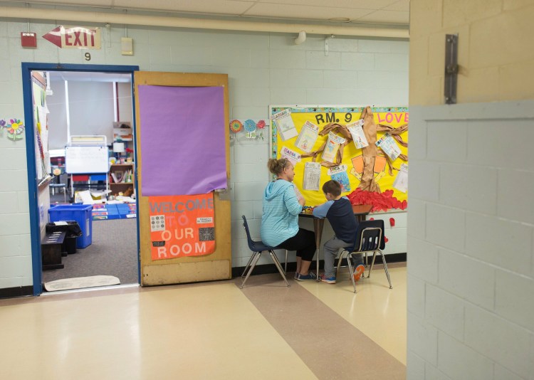 Stacey Mooney, an ed tech, works with a student at a table in the hallway at Lyseth Elementary School on Tuesday. The school has run out of room so Mooney works with some children in the halls. 