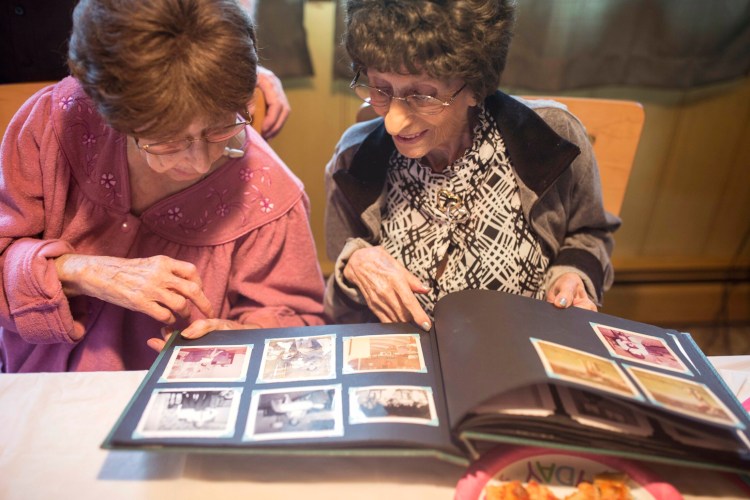 Mary Pizzo McCarthy, left, and Amelia "Millie" Pizzo Lane look at old photo albums while celebrating their 100th birthday at Mary's home in Portland on Wednesday. The twins were born in Italy and immigrated to Portland with their parents in 1929. 