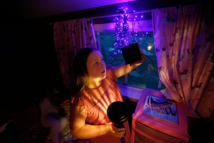 Sera Dixon, 9, holds a solar light in her right hand while demonstrating a solar panel with her left in the bedroom she shares with her twin sisters. The family has been using solar lights to cut down on electricity costs. 