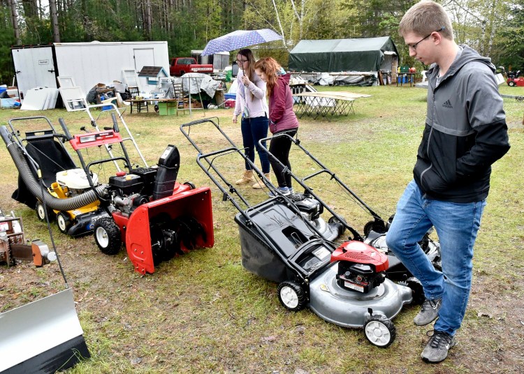 Brady Murray looks over lawn mowers for sale Sunday at a residence in Skowhegan during this year's 10-Mile Yard Sale. His friends Alyssa Watrous, left, and Cassidy Hamm also look around for deals.