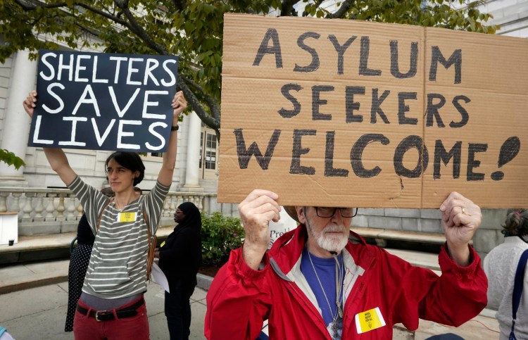 Peter Carleton, right, holds a sign in support of asylum seekers and Casey Ryder holds a sign in support of the city’s shelter during a rally at Portland City Hall Monday. The two Portland residents were among over 100 people at a rally protesting potential cuts to the city budget. 