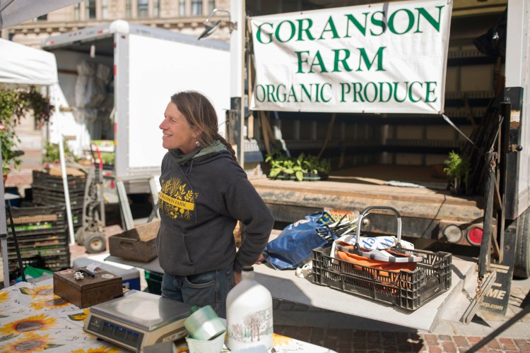 Jan Goranson mans the Goranson Farm stall at the Portland Farmers' Market in Monument Square on Wednesday. Goranson, one of the owners of the family farm in Dresden, said a chilly, rainy spring has made farming "challenging to say the least." 