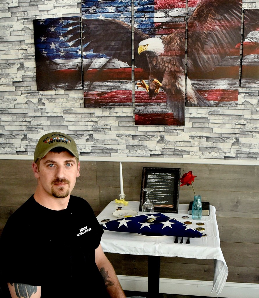 Veteran Derek DeFelice sits on Wednesday at the Fallen Soldiers Table at his Hero's House of Pizza in Skowhegan. DeFelice, who will be the grand marshal of the Skowhegan Memorial Day parade this Monday, created the table in honor of veterans who died fighting in wars. 