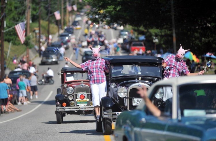 Pat Knowlton, center, and Kathie Blodeau , right, hang from the Pat's Wallpaper antique car dressed as pigs with pinwheels in the Blueberry Festival parade on Main Street in downtown Wilton in August 2012. 
