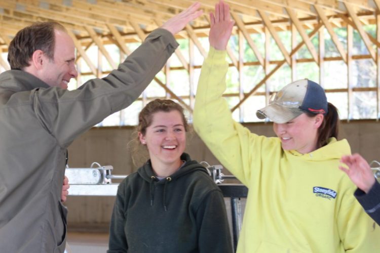 David Herring, executive director of the Wolfe’s Neck Center for Agriculture and the Environment, high-fives dairy farmer apprentices Corinne Carey, left, and Tierney Lawlor at the grand opening of the center’s organic dairy facility Thursday. Herring directed everyone to celebrate the opening with high fives in lieu of a ribbon cutting.