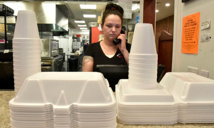 Waterville House of Pizza Manager Ashley Ann Ferris speaks on the phone near stacks of styrofoam products used for take-out orders on Thursday. Owner Stavros Kosmidis said he understands the benefit of banning plastic, but the cost is not ideal.