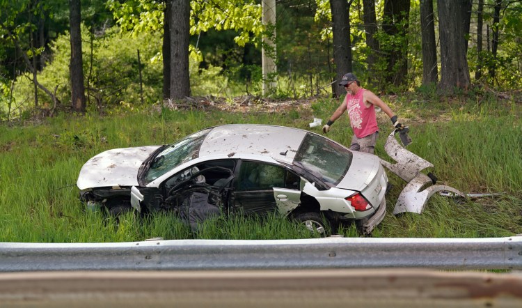 A man picks up debris around a car that went off the southbound lane of the Maine Turnpike in Scarborough on Tuesday.