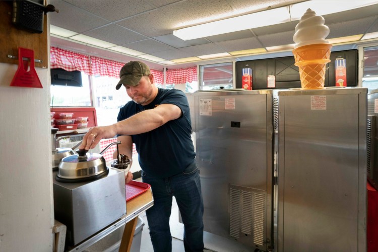 Jason Curtis, who owns Island Dairy Treat in Skowhegan with his wife, Shannon, pours hot fudge on an ice cream order while working at the shop in June. Central Maine Power bills for the ice cream shop jumped from $600 to over $900 a month, and Curtis says nothing in the 200-square-foot shop had changed. He said the billing issues still have not been resolved with CMP. 