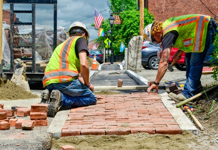 Sargent Corp. workers Ryan Modery, left, and Dustin Dugan build a narrower sidewalk Thursday in front of the Lucky Garden restaurant's parking lot along Water Street in Hallowell.