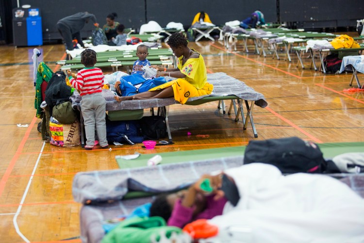 Families rest on cots in June at the Portland Expo, which the city opened as a temporary emergency shelter for asylum seekers. In about two weeks, The Expo will revert to its role as a sports arena.
