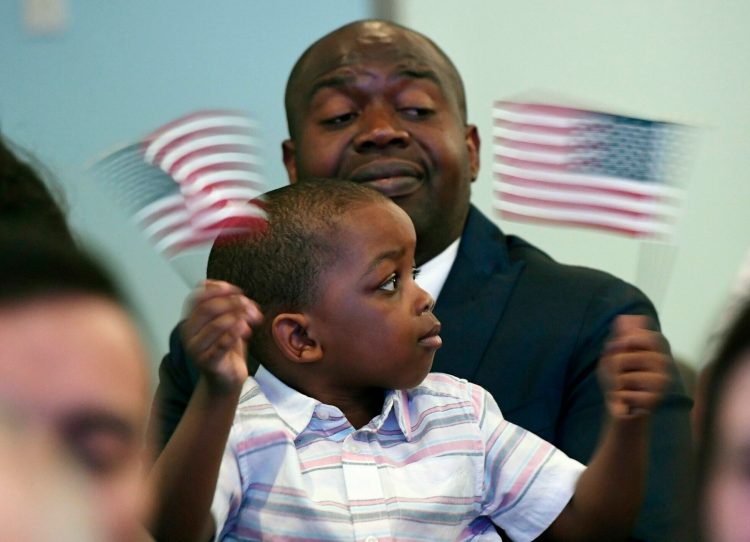 Jefferson Binda of Portland holds his son Jallen, 3, as Jallen waves flags during the naturalization ceremony at the Portland Public Library on Friday. Binda, originally from the Democratic Republic of the Congo, now lives in Portland with his wife, Eliane Binda. 