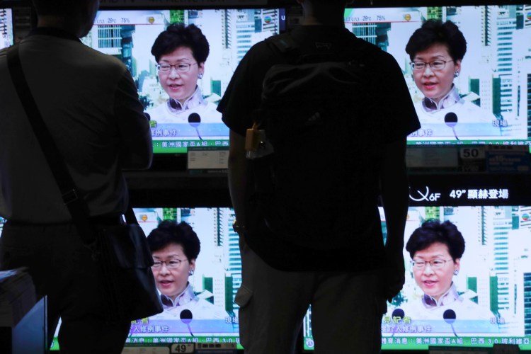 Residents watch a broadcast of Hong Kong Chief Executive Carrie Lam speaking at a press conference Saturday. Lam is suspending an extradition bill indefinitely after widespread public protests. The measure would enable authorities to send some suspects to stand trial in mainland China. 