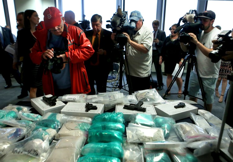 Members of the media take photos of guns, drugs and money on display at a news conference Thursday in Boston. Authorities said they arrested 14 people and seized more than 53 pounds of fentanyl, heroin and cocaine in the bust of a major drug trafficking ring.  