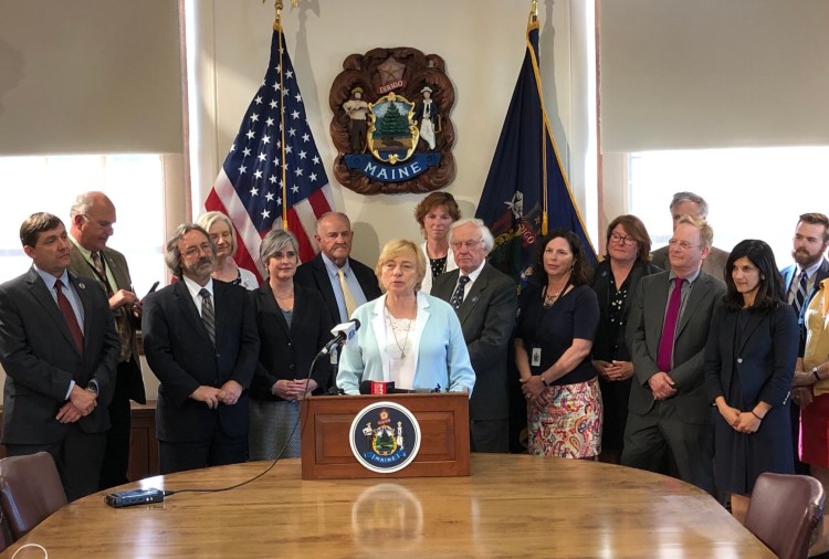 Gov. Janet Mills is surrounded by legislative leaders and bipartisan members of the budget-writing committee Monday as she prepares to sign a two-year, nearly $8 billion budget.