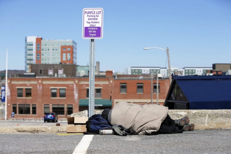 In April, a man sleeps in a parking lot near the Oxford Street Shelter in Portland. A proposal calls for building a new city shelter away from the concentrated homeless services in Bayside.