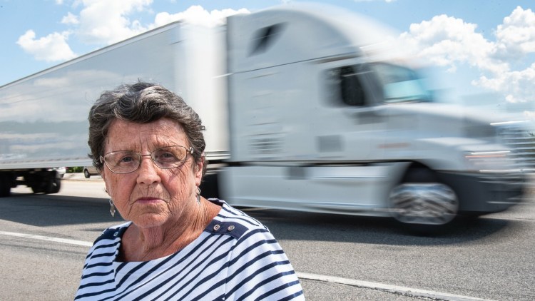 Daphne Izer watches tractor-trailers fly past on their way to the Maine Turnpike at the Auburn interchange Tuesday. Izer started Parents Against Tired Truckers in 1994, after her son and three of his friends were killed when a truck driver fell asleep and hit their car in the breakdown lane on the Maine Turnpike.