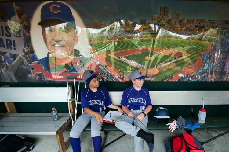 Waterville teammates Camden Brown, left, and Cormac Wilcox sit under a mural of Fran Purnell, whose name graces the Wrigley Field replica, during an 11U Cal Ripken state tournament game against Gardiner earlier this month. Waterville will host the 11U New England regional, which begins this weekend.