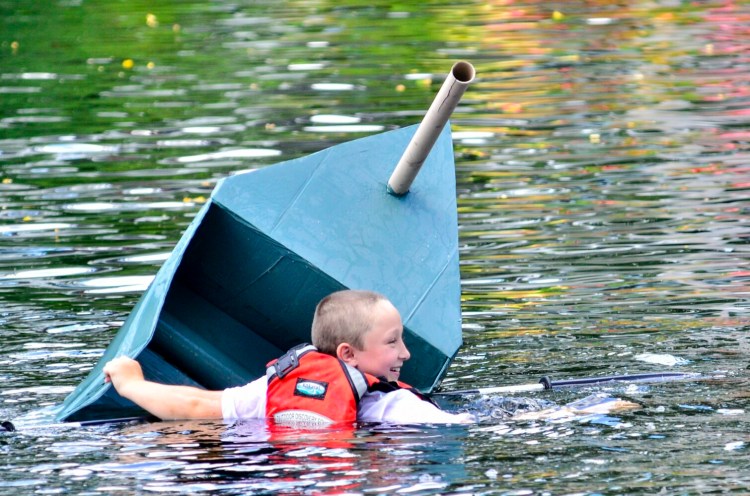 Isaac Stevenson swims in Mill Pond after his cardboard boat, S.S. Tuna, sank Saturday during a race at the Strawberry Festival in Wayne. 