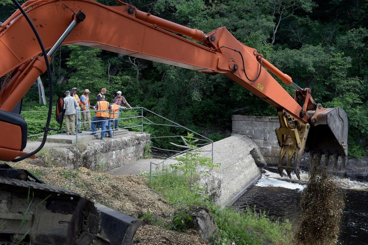 An excavator spreads wood chips Tuesday at the base of the Head Tide Dam in Alna, as construction begins on a modification of the dam's passages on the Sheepscot River. 