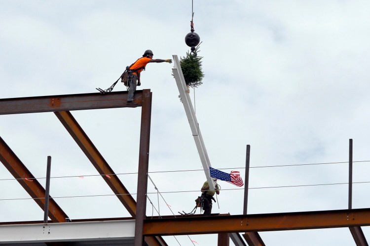 Sean Nolan, left, and Nick Andrews of Bouchard Steel Erectors lay the final beam on the main structure of Hobson’s Landing on Wednesday. The project is being built on the former site of Rufus Deering Lumber Co. on Commercial Street in Portland. The beam was adorned with a traditional pine tree for good luck and an American flag. 