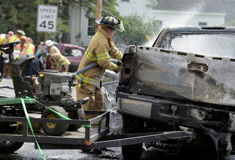 A firefighter extinguishes a burning pickup truck as colleagues extricate the driver of another pickup after the vehicles collided Wednesday on U.S. Route 201 in Richmond. Witnesses and neighbors removed the driver of the burning pickup moments before it exploded in flames.