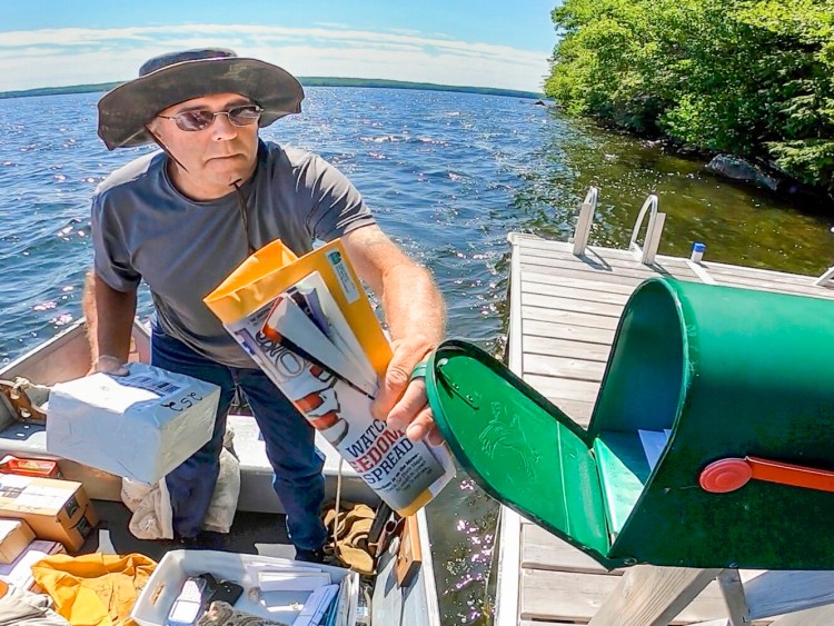 John Govostes Jr. opens a mailbox July 25 to put in a package on his watery route on Great Pond in Belgrade.