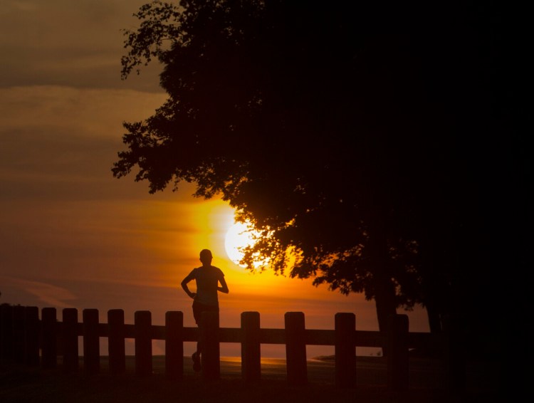 The sun rises behind a runner at Fort Williams Park in Cape Elizabeth on Tuesday. July was consistently warm this year, with a vast majority of the days a few degrees above average.