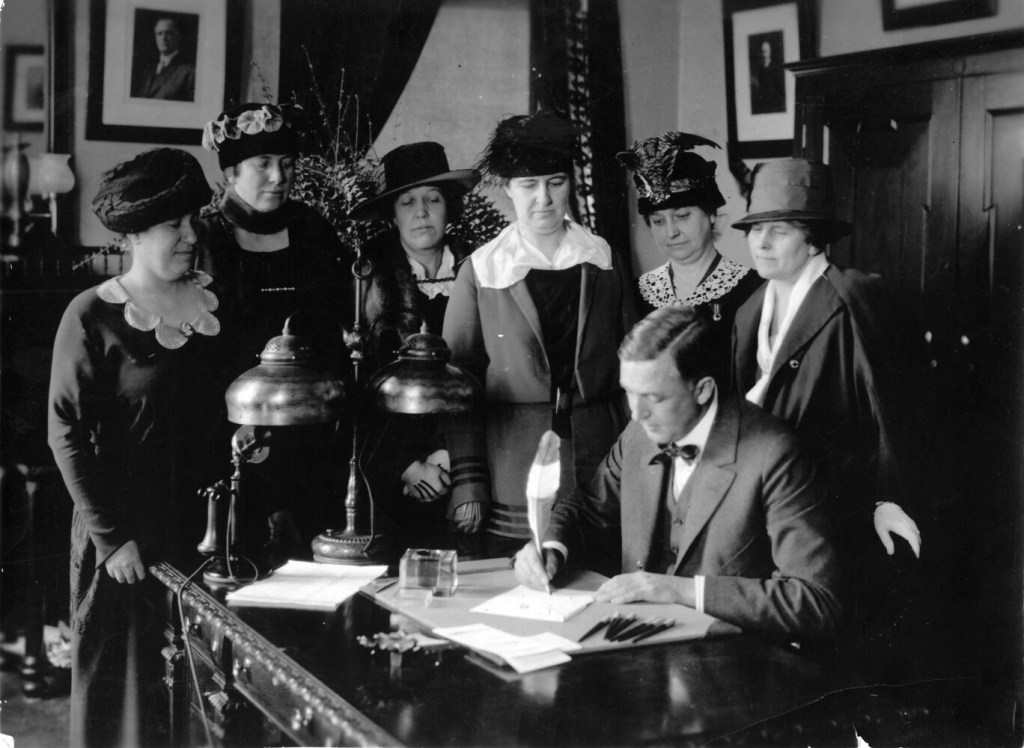 Gov. Carl Millikin signs the ratification of the 19th amendment. From right to left: Florence Brooks Whitehouse, chair, National Women’s Party Maine branch; Grace Hill, NWP Maine branch; Mabel Connor, Maine Woman Suffrage Association; Katherine Reed Balentine, MWSA Legislative Committee chairwoman, Gertrude Pattangall, MWSA corresponding secretary, and Anne Gannett, president of the Augusta Woman Suffrage Association.
