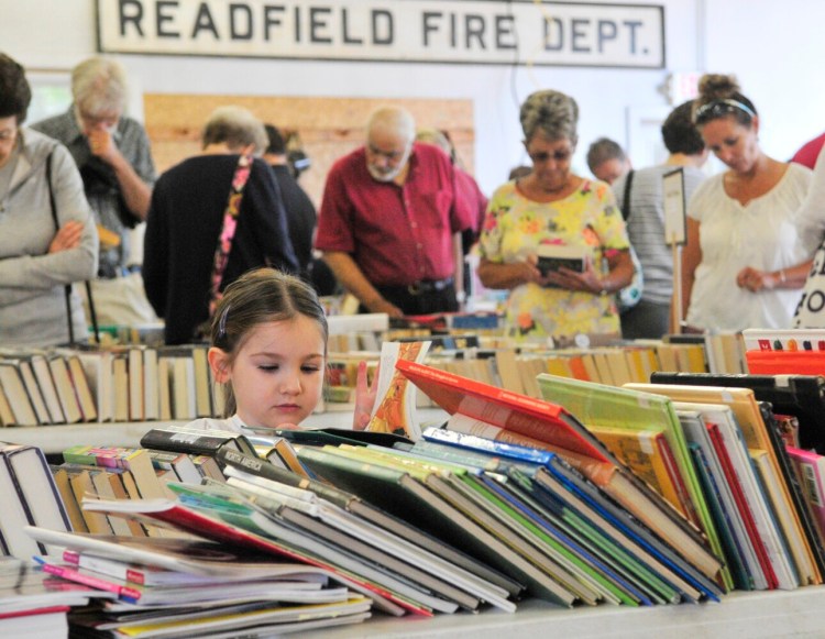 While adults browse in the background, Julia Henderson reads her book during the Readfield Community Library book sale in August 2015, during Readfield Heritage Days.
