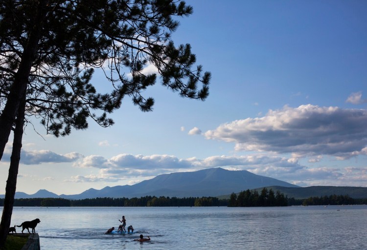 Mount Katahdin looms in the background as children play on a raft at New England Outdoor Center, situated on Millinocket Lake, last August.