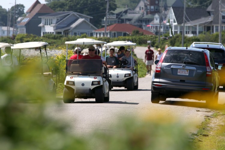 Rented golf carts squeeze through a narrow lane between passing cars and other parked golf carts on Seashore Avenue on Peaks Island on Wednesday. 