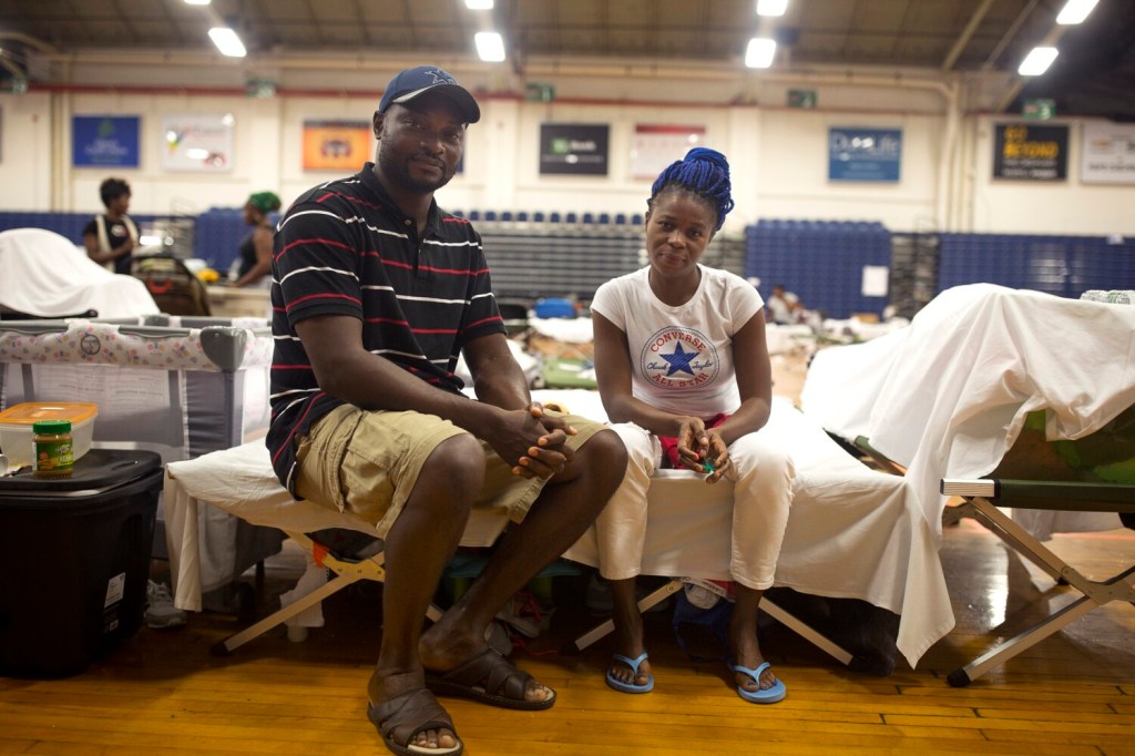 Mao, left, and Makina pose for a portrait on their cots at the Portland Expo on Wednesday. The couple, along with all of the other asylum seekers left at the Expo, are packing up their belongings to move out. Mao, Makina and their two daughters are moving in with a host family in Brunswick .