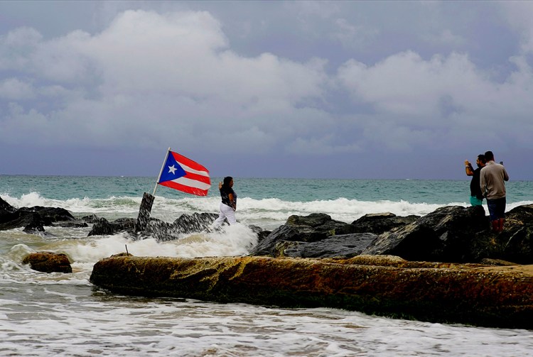 A woman poses for a photo in front of ocean waters and a Puerto Rican national flag, after the passing of Tropical Storm Dorian Wednesday in the Condado district of San Juan, Puerto Rico,