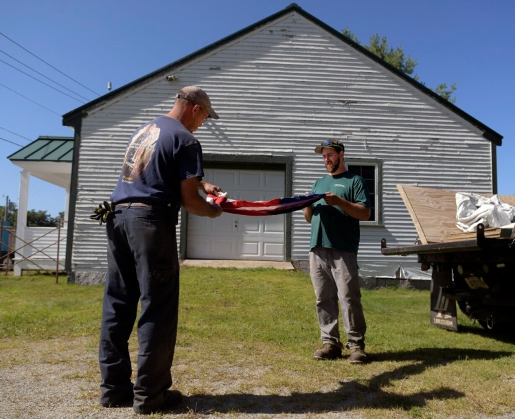 Chase Nutter, right, and Chris Dutill fold an American flag Sept. 18 that was recovered from Belgrade Town House. Nutter, a seasonal maintenance worker for the town, and Dutill, who manages the town's facilities and serves as the sexton, removed contents of the 19th-century structure ahead of restoration work.