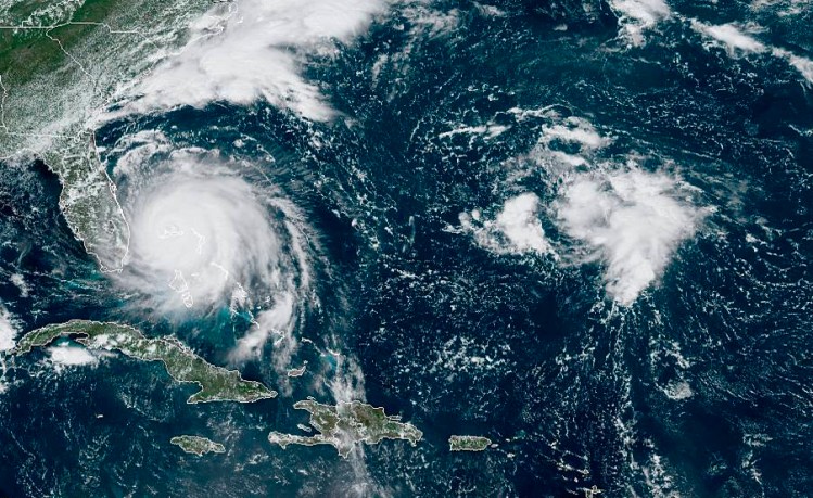 This satellite image taken early Monday afternoon and provided by National Oceanic and Atmospheric Administration shows Hurricane Dorian, left, churning over the Bahamas.