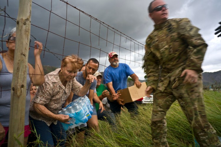 A Puerto Rican National Guard member delivers food and water brought by helicopter in the San Lorenzo neighborhood of Morovis, Puerto Rico, two weeks after Hurricane Maria hit in 2017. Money to rebuild a National Guard base in Puerto Rico is being redirected to build Trump's border wall. 