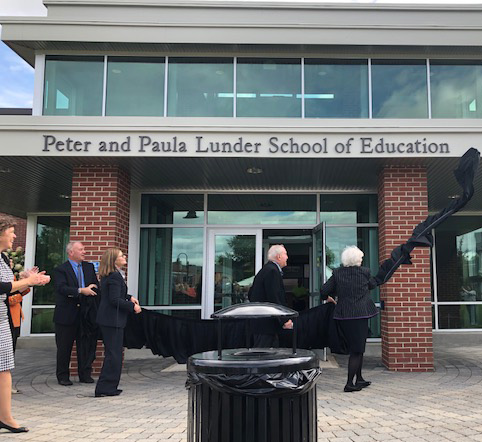 Thomas College President Laurie Lachance, left, applauds the unveiling of the signage naming the Peter and Paula Lunder School of Education at Thomas College in Waterville on Monday. Kevin Gillis, second from left, president of the Lunder Foundation and nephew to the Lunders, and the couple’s daughter, Margie Lunder, assist Peter, second from right, and Paula Lunder, right, as they uncover the name on the building. 