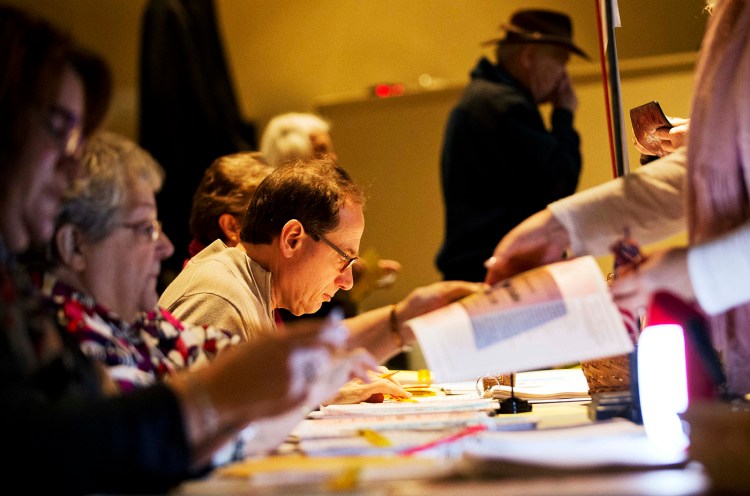 Election officials assist voters lining up to cast their ballots at a polling site for the New Hampshire primary in 2016 in Nashua, N.H. 