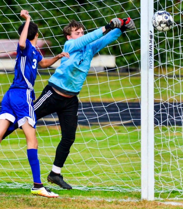 Hall-Dale keeper Sam Sheaffer, right, deflects a shot in front of Mt. Abram senior Jed Zelie during a game on Wednesday at Hall-Dale High School in Farmingdale. 