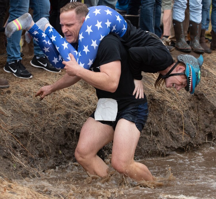 Jesse Mead carries his wife Amy through the water obstacle Saturday  at Sunday River in Newry. The Portland couple finished in fourth place.