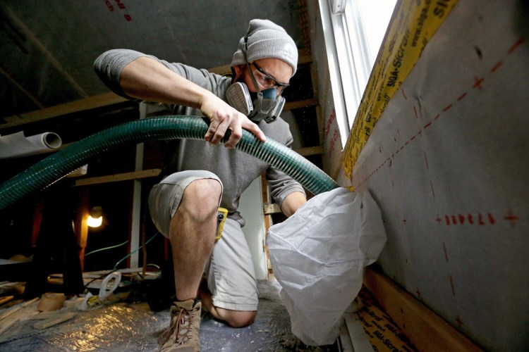 Cody Moreau, a worker from Horizon Homes, uses a hose to blow fill bays encased in a membrane with insulation in an attic in South Portland in this file photo from 2019. An updated statewide energy code for new homes and commercial buildings in Maine takes effect July 1.