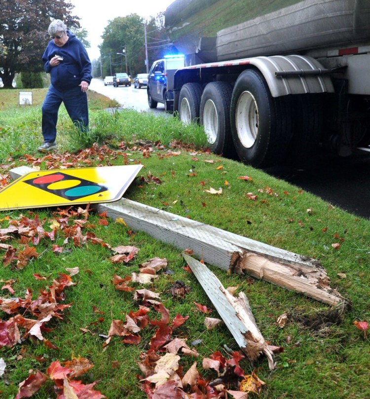Pat Finnimore carries broken window glass that she picked up in her yard in the 400 block of North Main Street in Waterville after a two-vehicle crash Tuesday morning. A road sign, pictured in the foreground,  was sheared off in the accident. 
