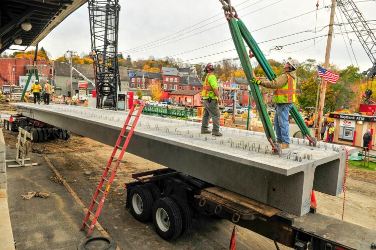 Workers rig straps from a large crane to the first of the new bridge supports put into place over Cobbossee Stream in downtown Gardiner in October. A commission formed to recommend new funding options for transportation projects will ask for more time to draft a long-term solution.